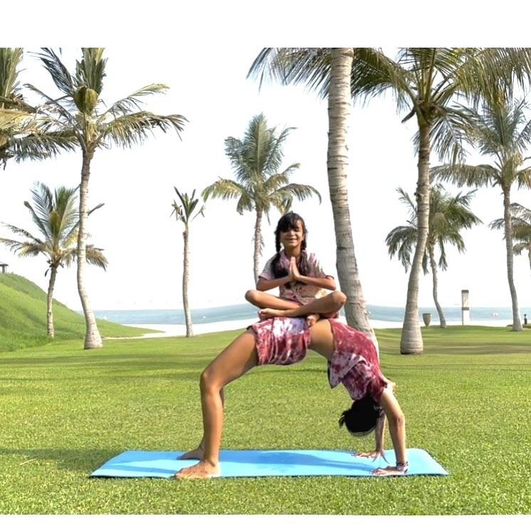 Aastha Chopra in Wheel, with her daughter on top (Urdhva Dhanurasana), Palm-lined lawn, Dubai, August 2021